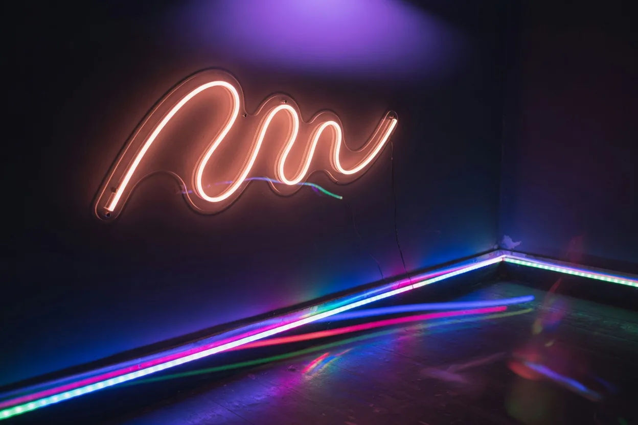 Superposition de lumières sur une piste de danse sombre : néon LED au mur, rubans RGB aux plinthes et halo de lumière noire violette